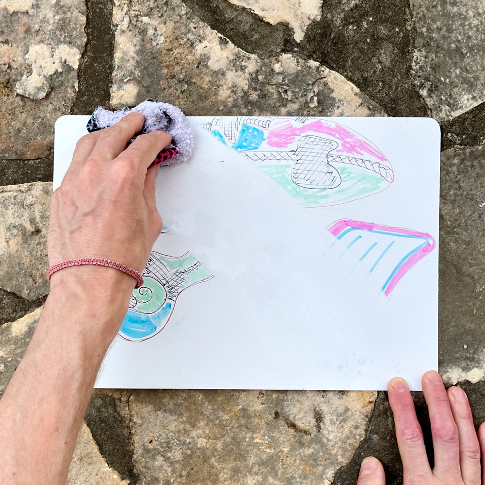 Hand holding a sheet with a colourful sketch in front of a stone wall.