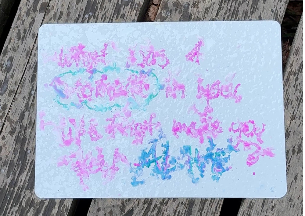 A written card covered in raindrops lying on a wooden table outdoors.