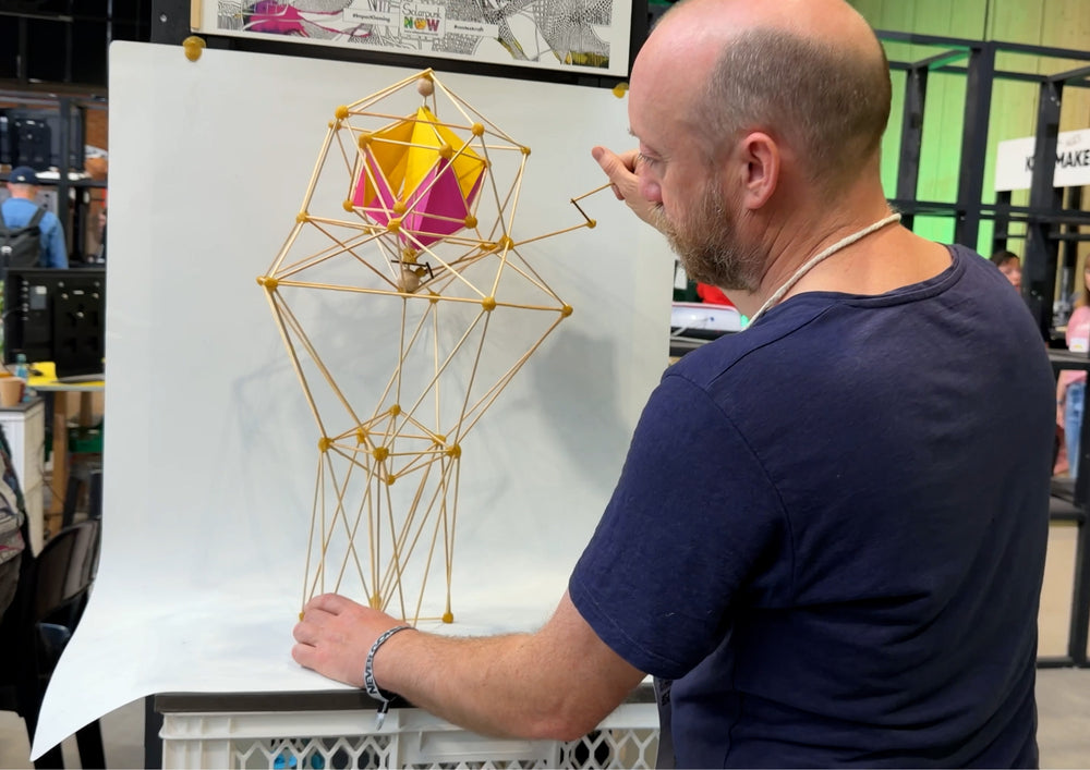 Man standing in front of a bamboo model that is attached to a large white sheet.