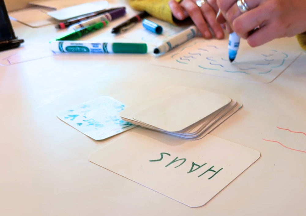 Hands drawing with felt tip pens on a large surface, a folded card standing in the middle.