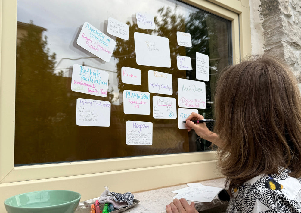 Woman writing on a card that clings to a window along with many others.