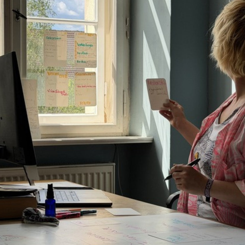 Woman standing at the window of her workplace reading a sheet, with more hanging on the pane.