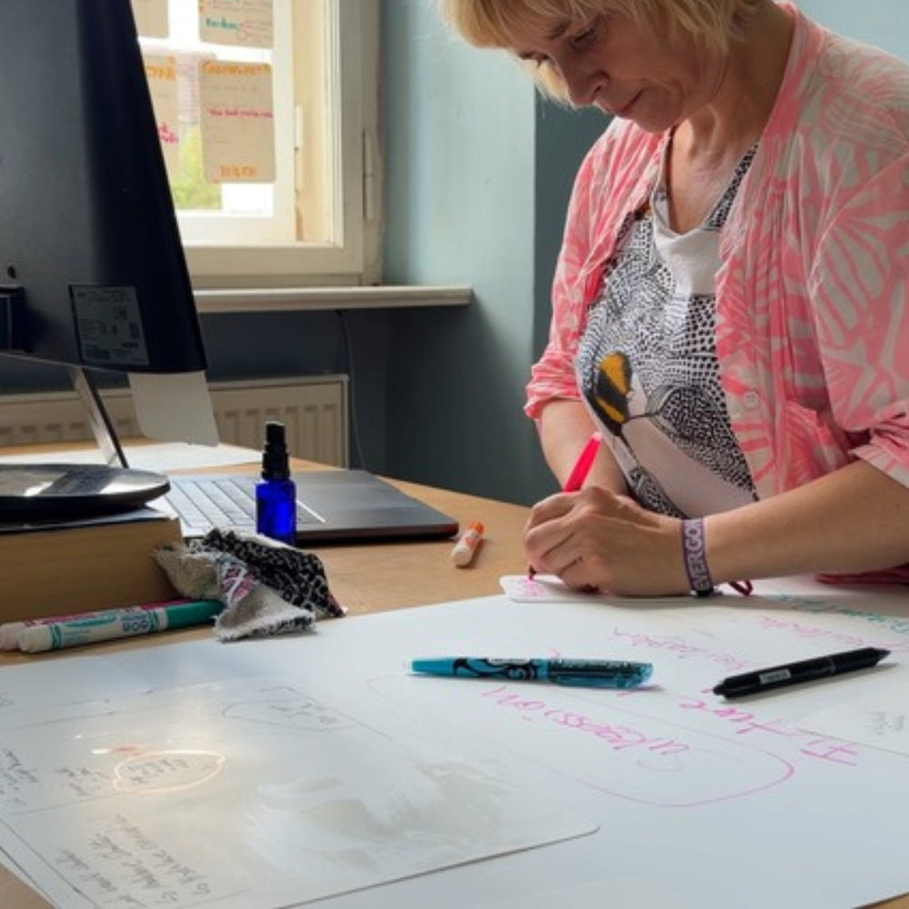 Woman at a desk drawing on a large sheet with felt tip pens.