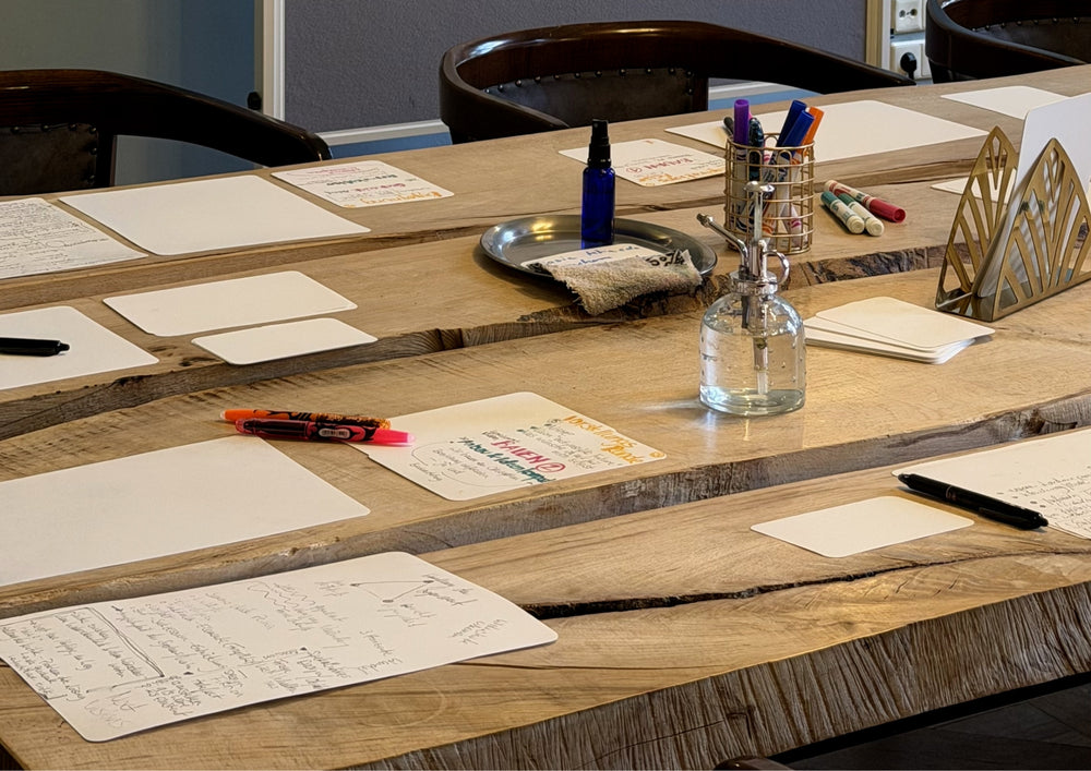 Long wooden table with written cards laid out, pens and a bottle of water.