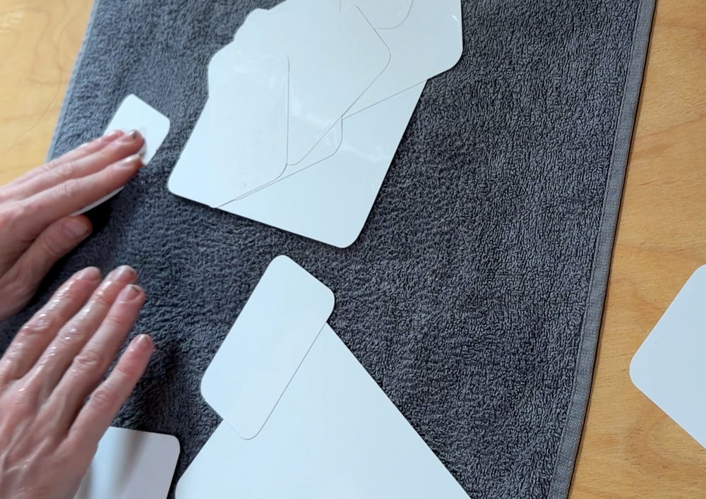 Hands wiping cleaned cards dry on a grey towel.