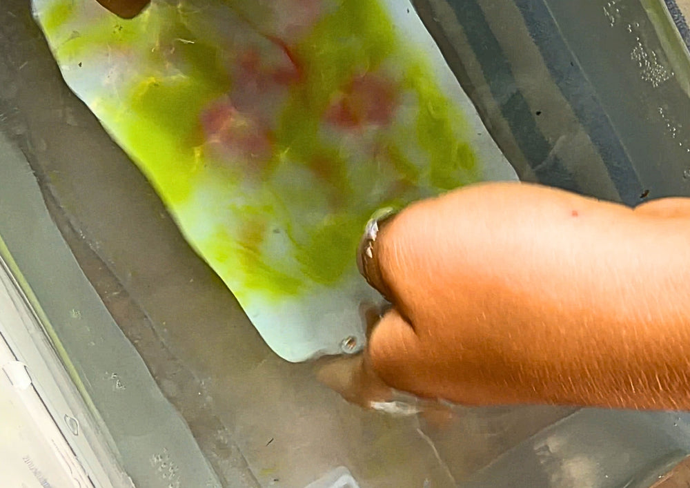 Hand dipping a painted card into a tub of water, the colour dissolves.