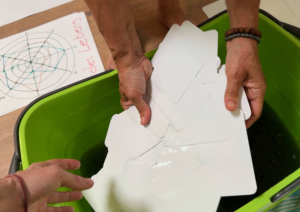 Two hands washing a stack of cards in a green tub.