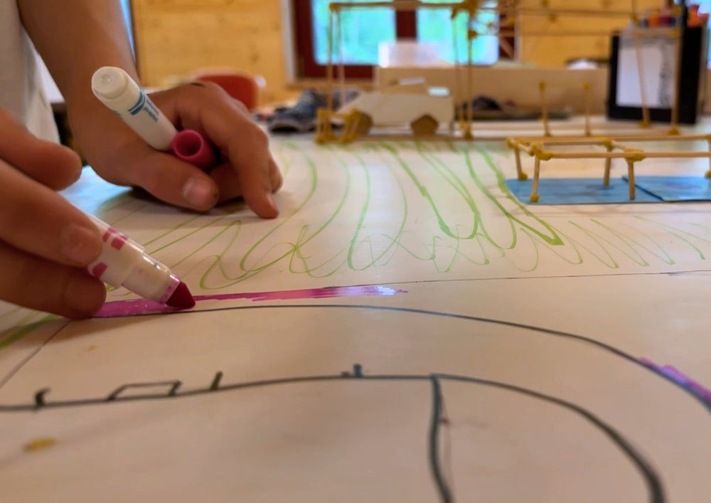 A child's hand drawing with a pen on a large sheet full of drawn lines.