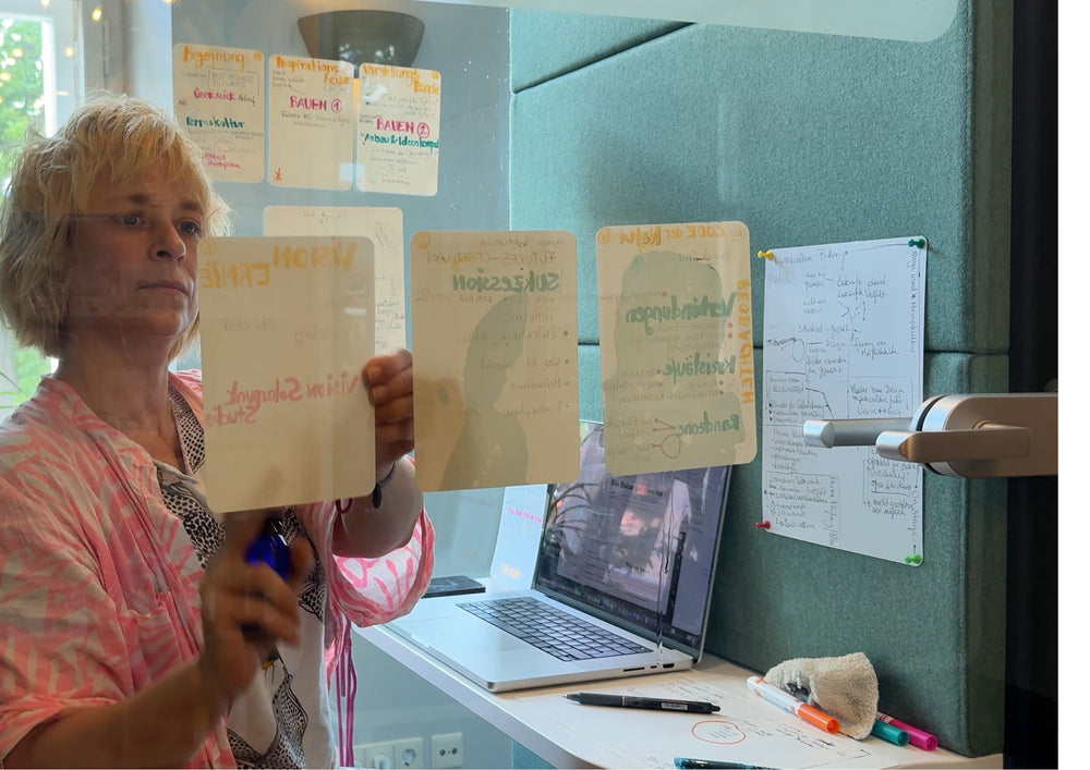 Woman holding up two written cards, more cards hanging on the window behind her.