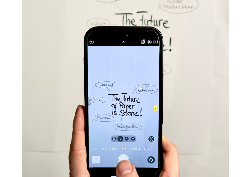 Hand holding a phone over a written sheet and photographing the handwriting.