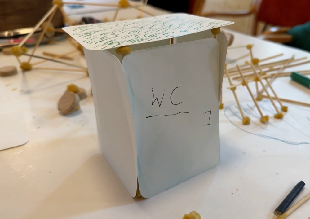 A folded card standing as a small house in the model, bamboo sticks lying beside it.