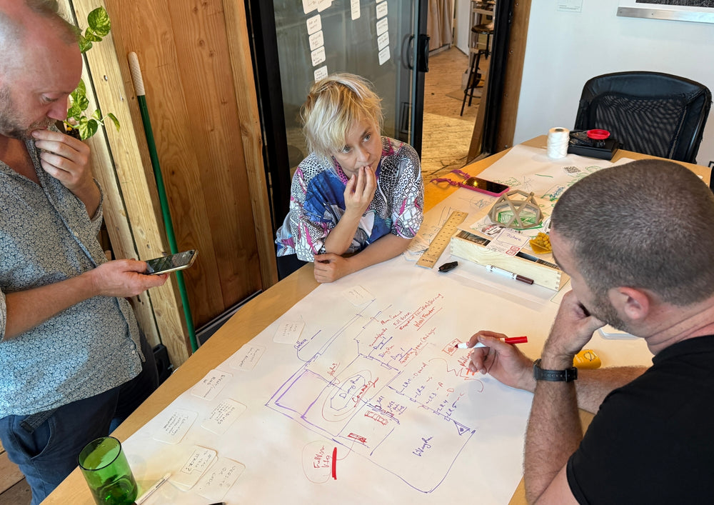Three people at a table, one writing on the shared sheet in the middle.