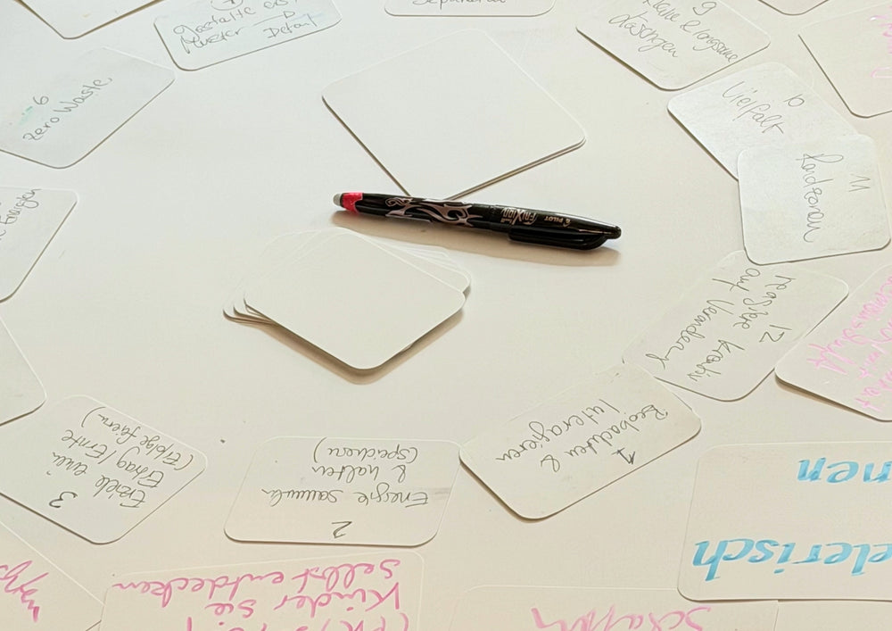 Written cards in several sizes spread out on a surface, a pen among them.