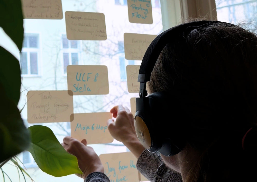 Person with headphones standing at a window pane and arranging written cards.