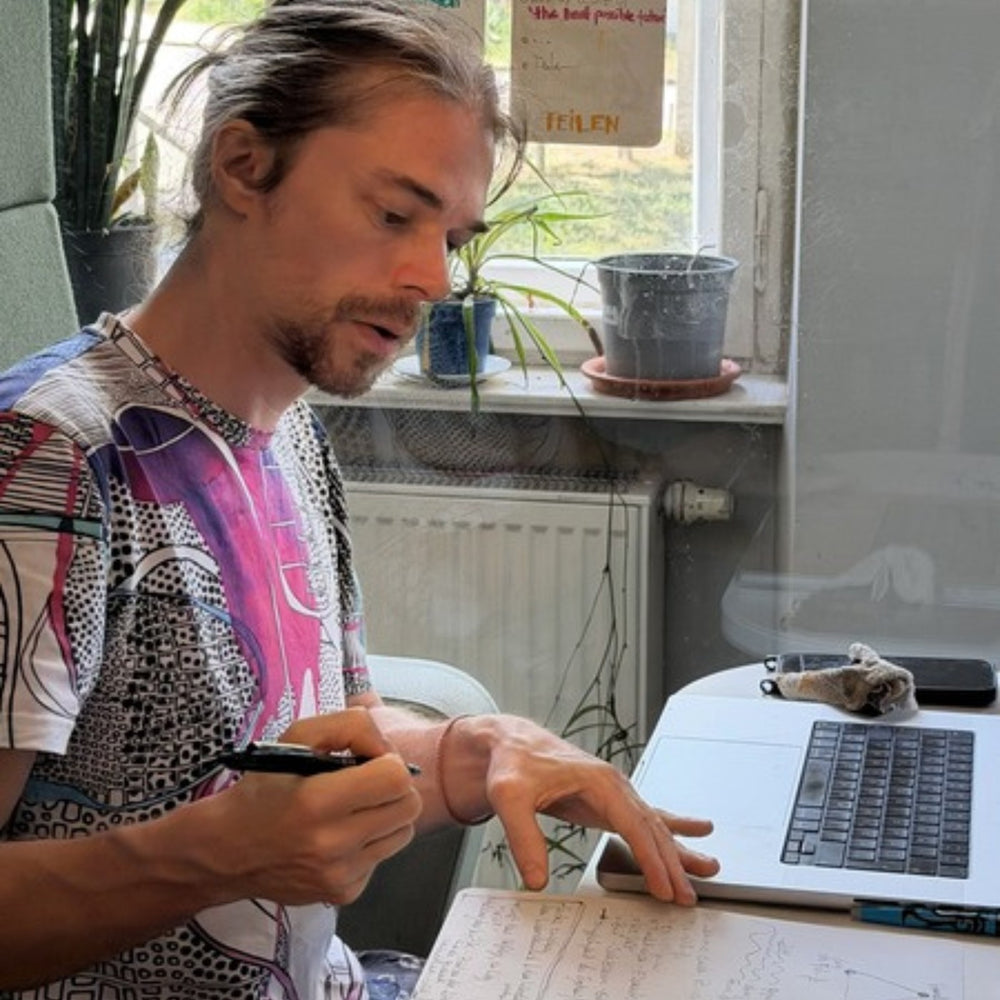 Man at a desk writing on a sheet next to an open laptop.
