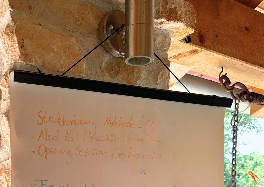 A written sheet hanging on a black magnetic rail in front of a stone wall.