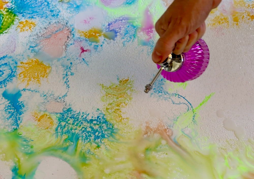 Hand spraying water from a bottle onto a colourfully painted surface.