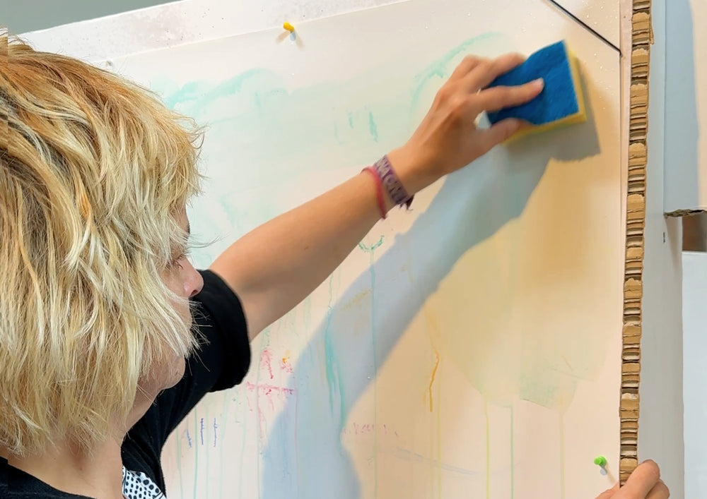 Woman wiping a large board on the wall with a sponge.
