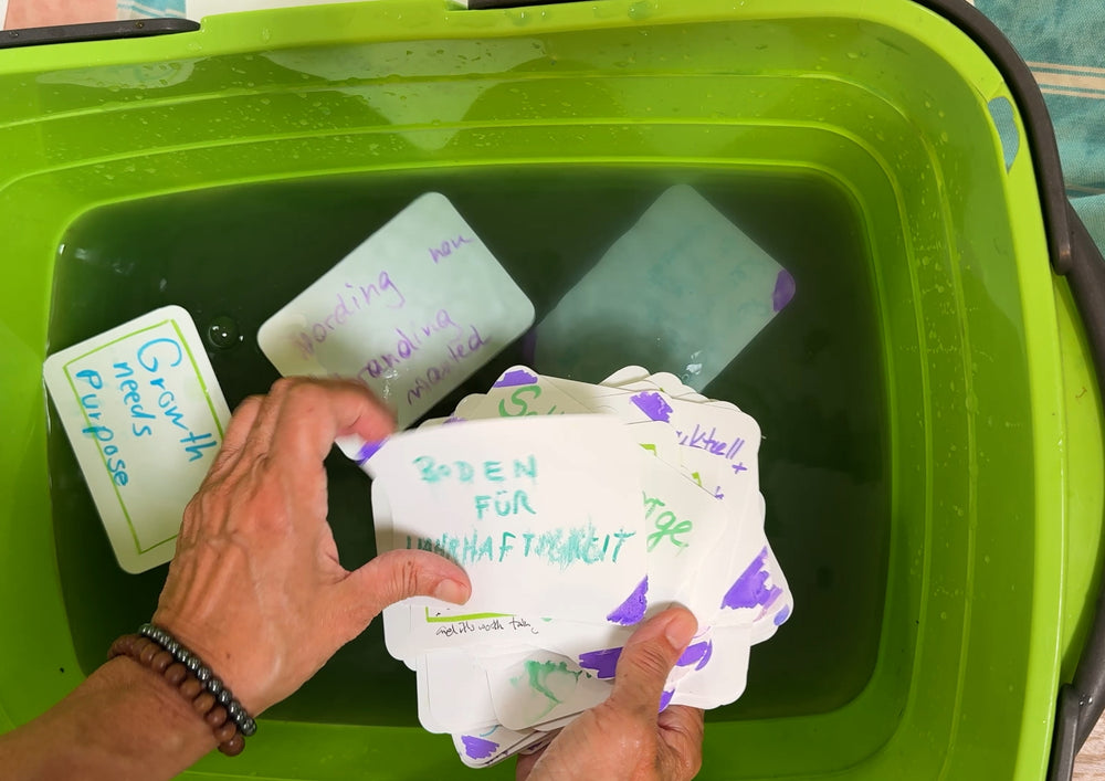 Hand placing written cards into a green bowl of water.
