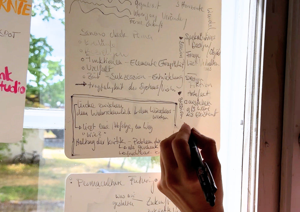 A hand writing while standing, on a sheet hanging upright at the window.