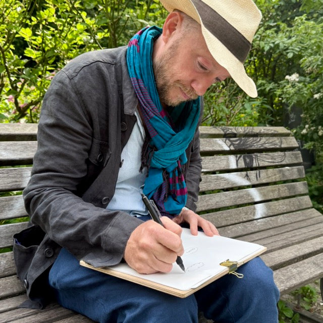 Man in a hat sitting on a bench and writing on a sheet on a clipboard.